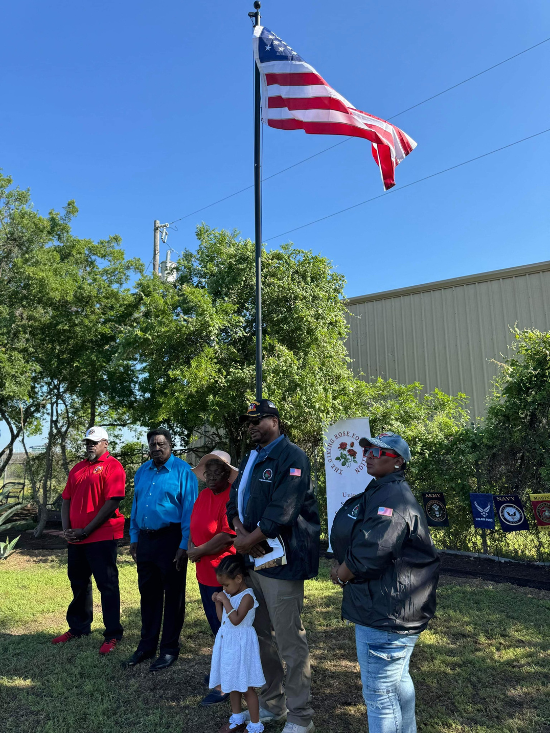 Community members and veterans gathered beneath the flag at a Giving Rose Foundation ceremony